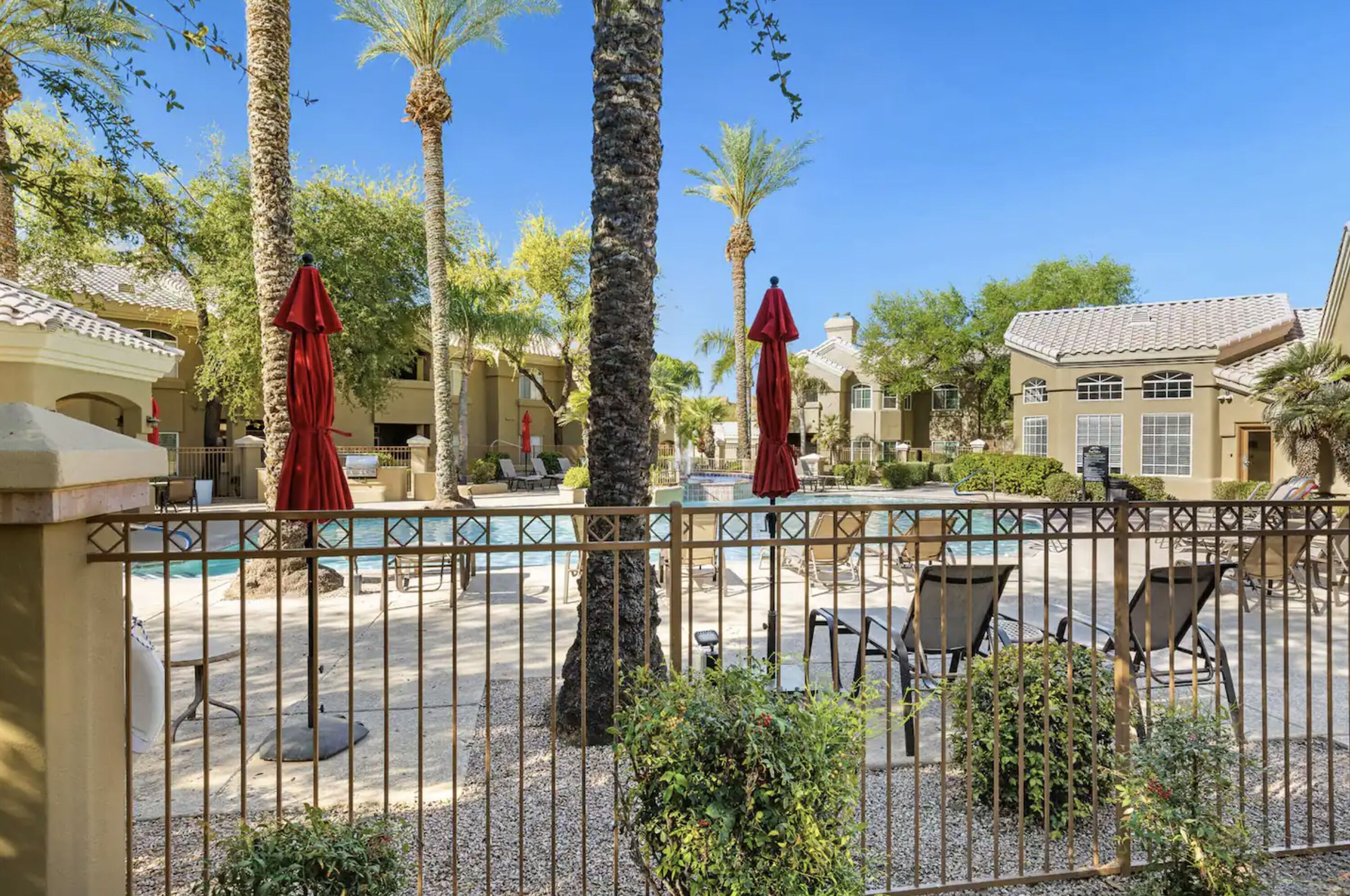 A pool area with palm trees, red umbrellas, and lounge chairs.