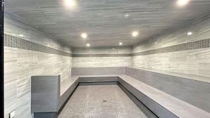 A modern, enclosed bathroom with tiled walls and floor, recessed lighting, and a bench along one wall. - Mt Green 3-f04 in Killington (Killington)