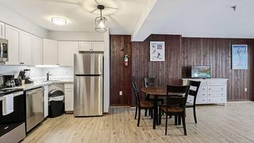 A modern kitchen with white cabinets, a stainless steel refrigerator, and a dining area with a wooden table and chairs.