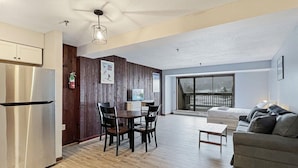 A modern apartment with a kitchen, dining area, and living room. It features a large sliding glass door to the balcony, a built-in wooden wall, and a stainless steel refrigerator. - Mt Green 3-f04 in Killington (Killington)