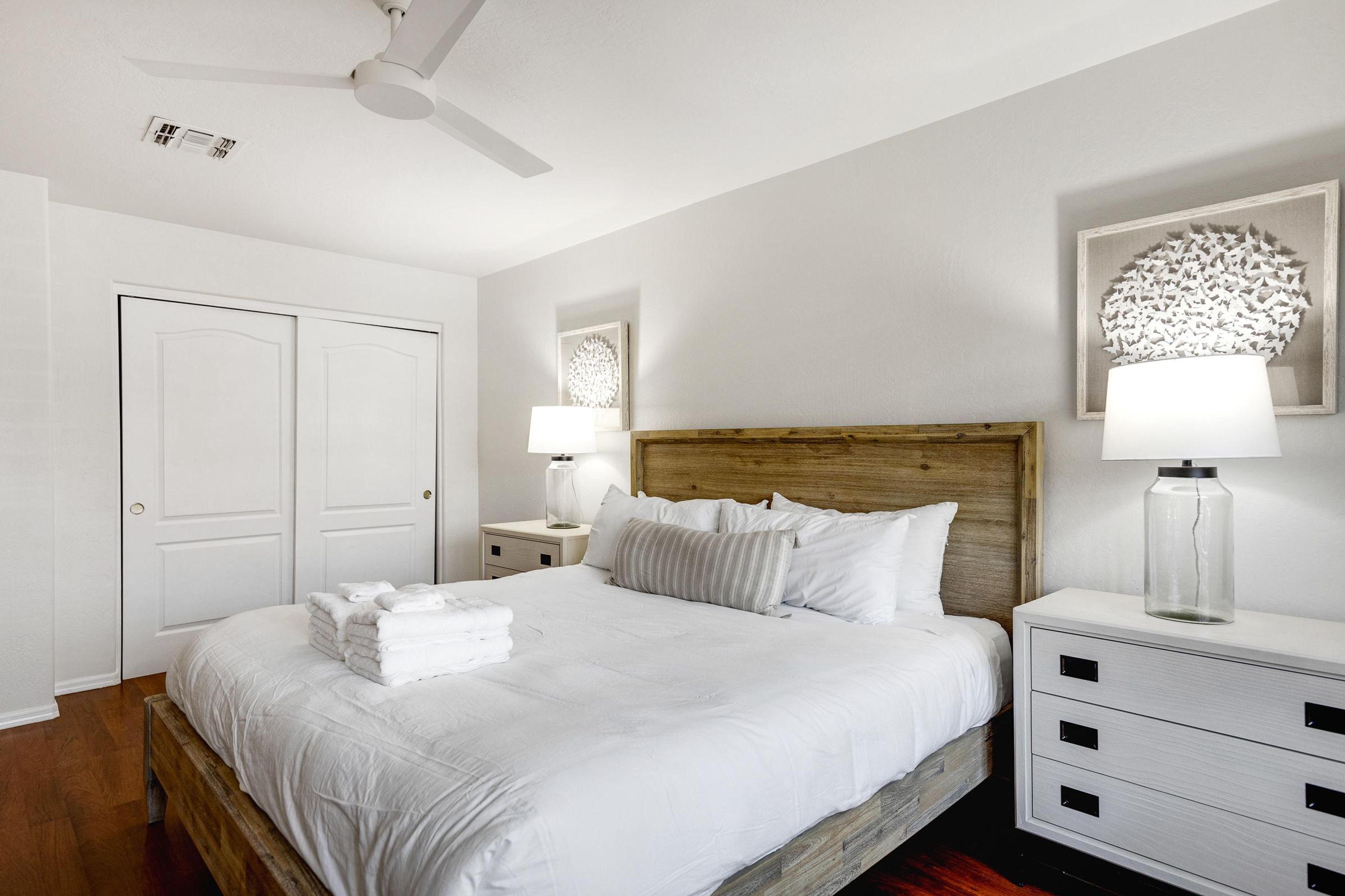A neatly arranged bedroom with a wooden headboard, a bed with white linens, a bedside table with a lamp, and a nightstand with a lamp.