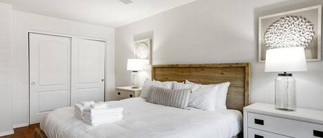 A neatly arranged bedroom with a wooden headboard, a bed with white linens, a bedside table with a lamp, and a nightstand with a lamp.
