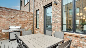 Une terrasse extérieure avec un mur en briques, un barbecue et une table avec des chaises.