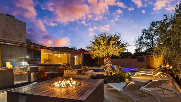 An outdoor kitchen with a built-in grill and fire pit, surrounded by lounge chairs and a swimming pool. - Chaparral in Paradise Valley (Paradise Valley)
