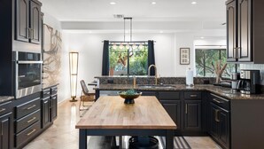A modern kitchen with dark cabinetry, a wooden dining table, and a view of greenery outside. - Chaparral in Paradise Valley (Paradise Valley)
