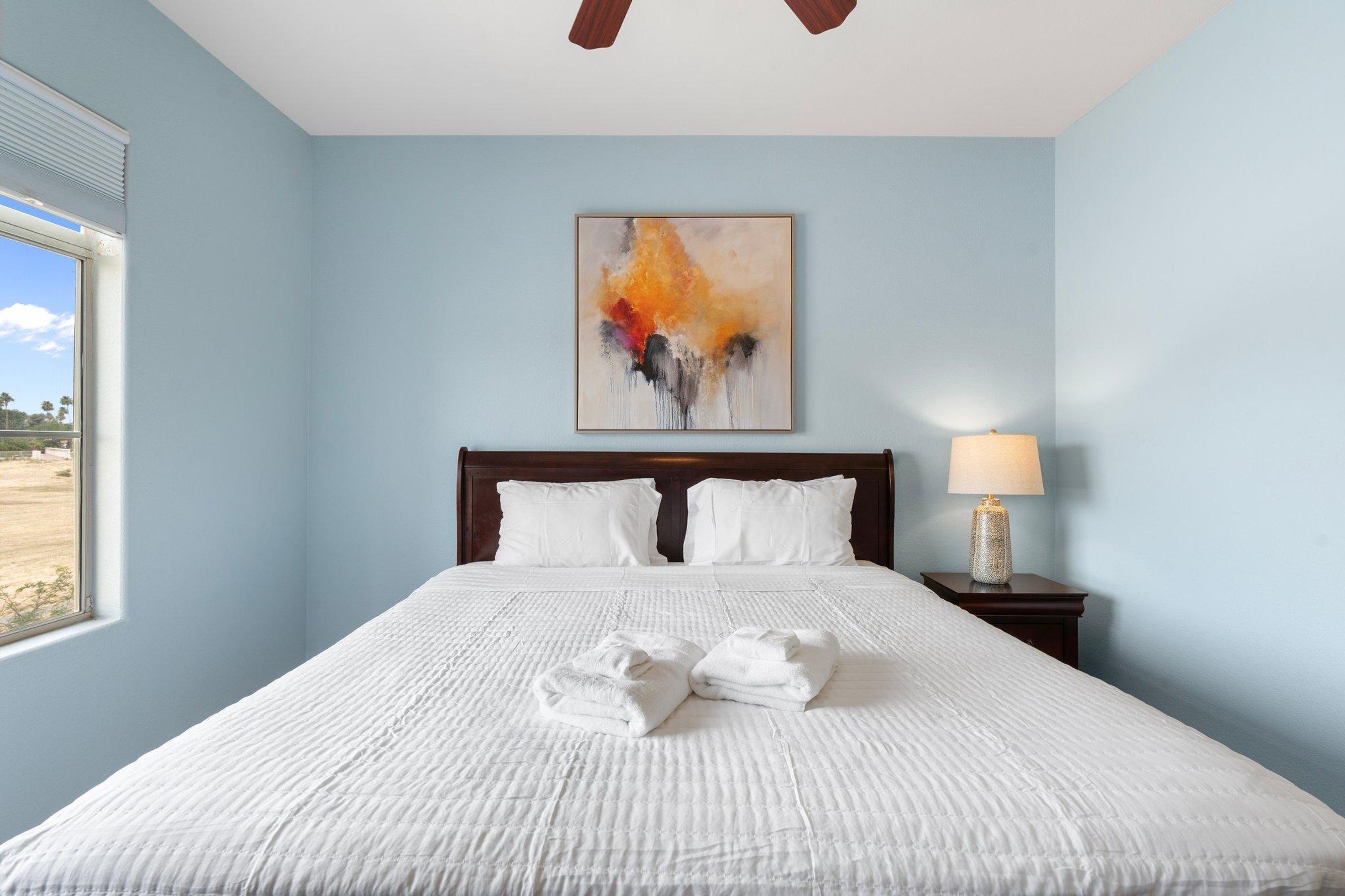 Een hotelkamer met een groot bed, witte lakens, een schilderij aan de muur en een raam met uitzicht.