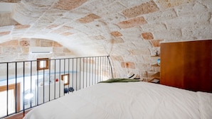 A bedroom with a stone ceiling, a balcony, and a bed with a green throw.