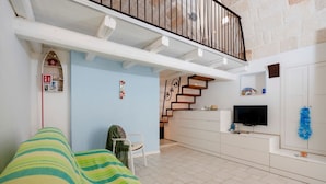 A living room with a sofa, a TV, a staircase, and a kitchen area.