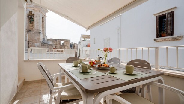 A balcony with a table set for breakfast, chairs, a railing, and a view of a historic building.