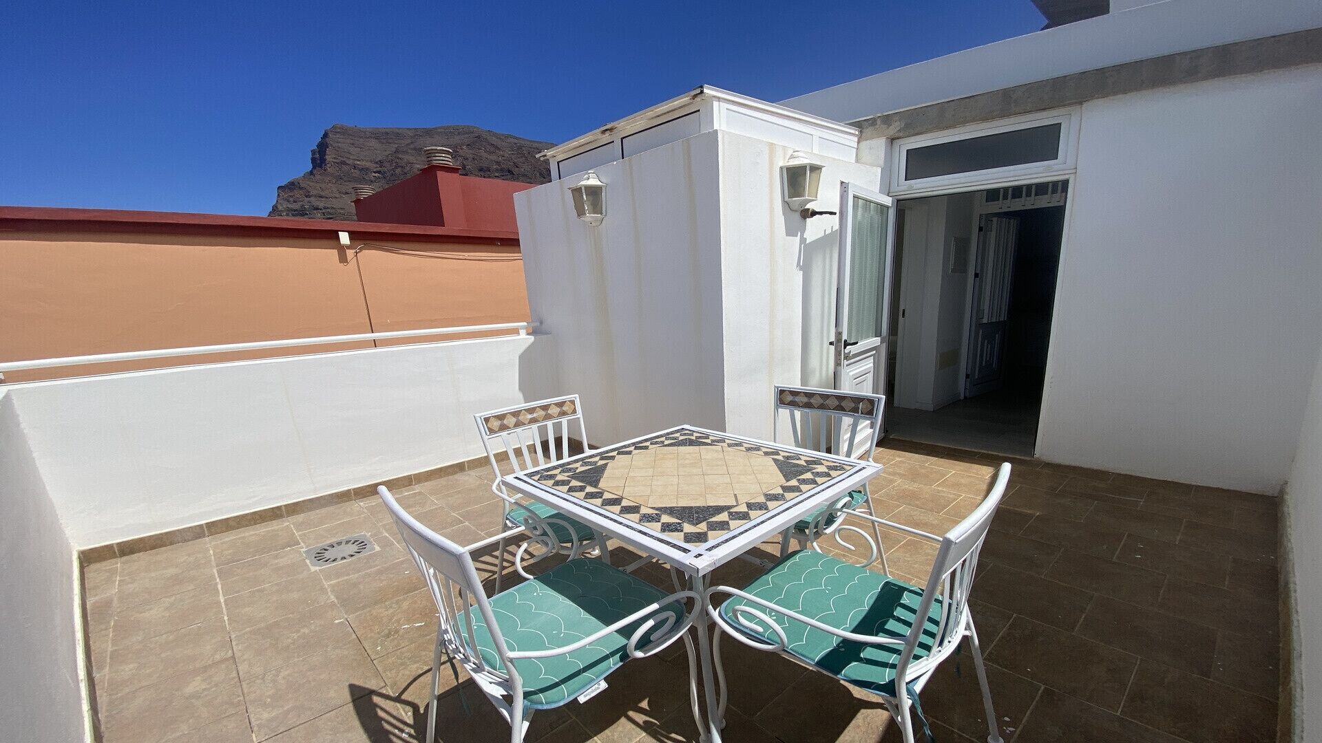 Un petit pati exterior amb una taula, cadires, una paret blanca i una porta que dona a l'interior.
