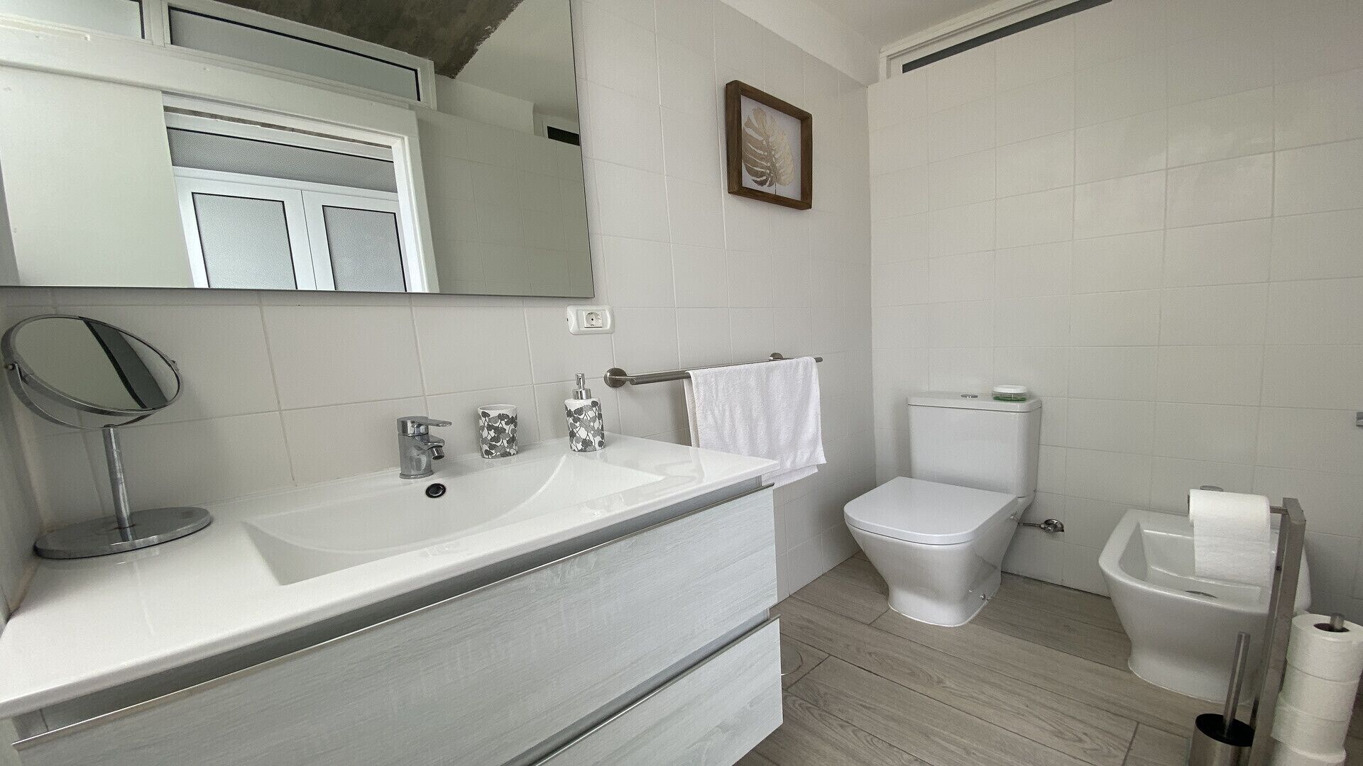 Een badkamer met een wit wastafelmeubel, spiegel, toilet en een lijst met een foto aan de muur.