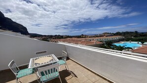 En balkong med ett bord och stolar, med utsikt över en swimmingpool och ett bostadsområde med hus som har röda tak.