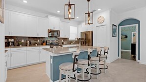 A modern kitchen with white cabinetry, a central island with bar stools, stainless steel appliances, and pendant lighting. - PLW4277 Summary:<br>Stor (Kissimmee)