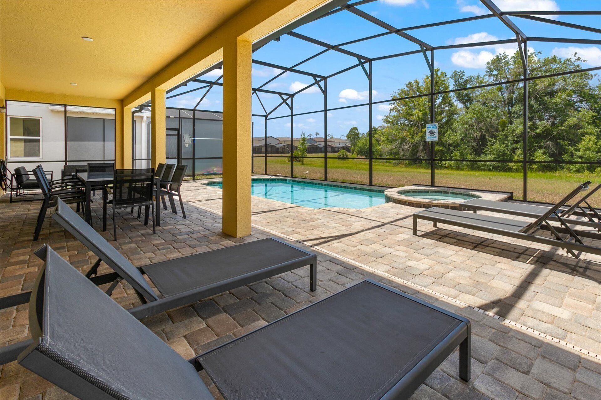Un espacio al aire libre cubierto con piscina, sillas de descanso y una mesa con sillas.