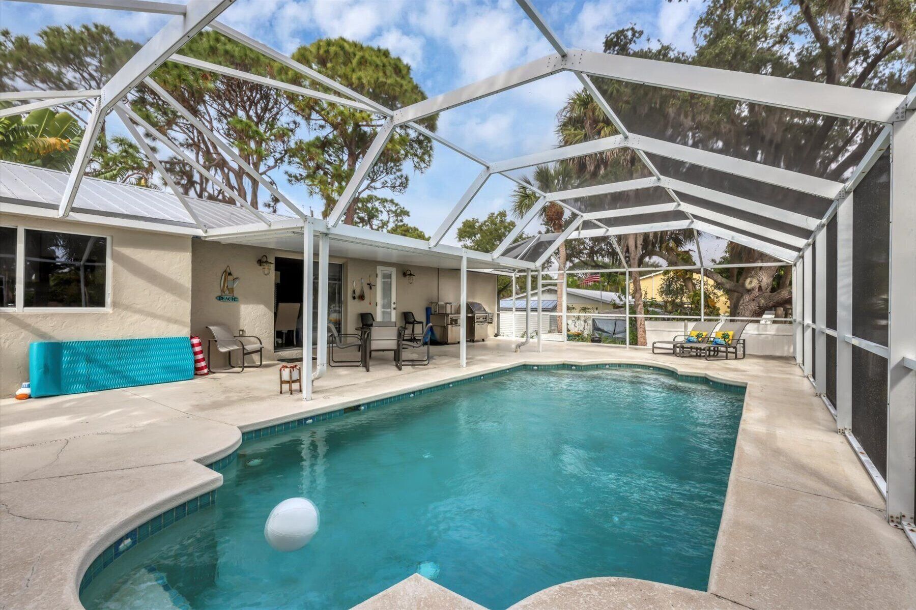 A covered swimming pool with a glass ceiling, lounge chairs, and a barbecue area.