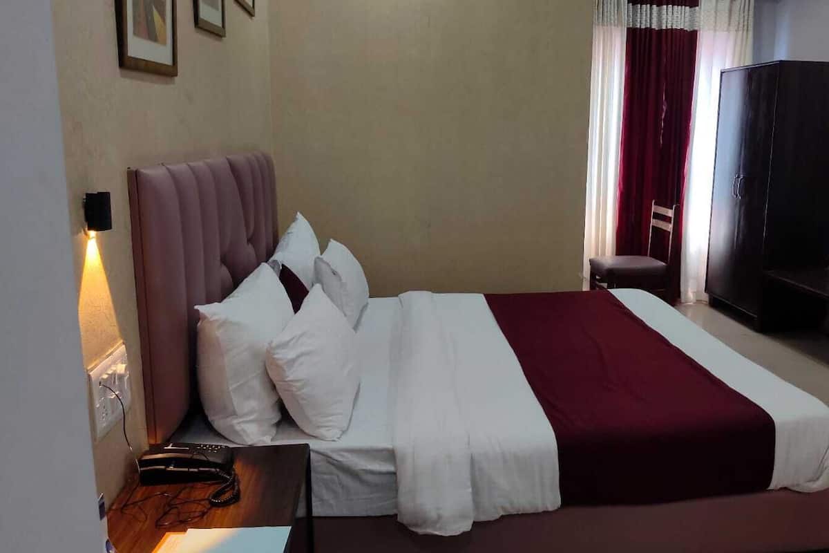 A neatly made bed with white and maroon bedding, a bedside table with a lamp, and a dark wooden wardrobe in a hotel room.