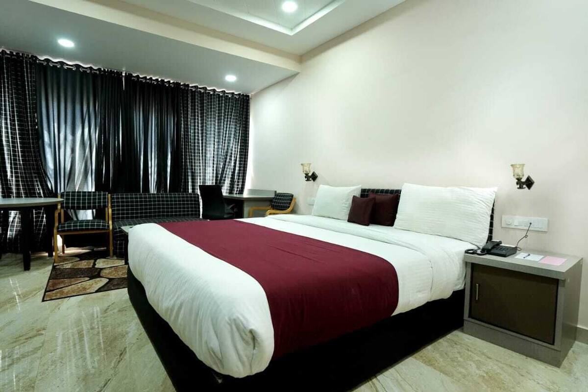 A hotel room with a large bed, a desk, a chair, and a nightstand with a lamp.