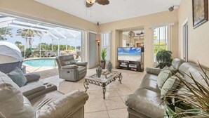 Ein großzügiger Wohnbereich mit Blick auf einen Pool, ausgestattet mit Ledersofas, einem Fernseher und einem Deckenventilator.