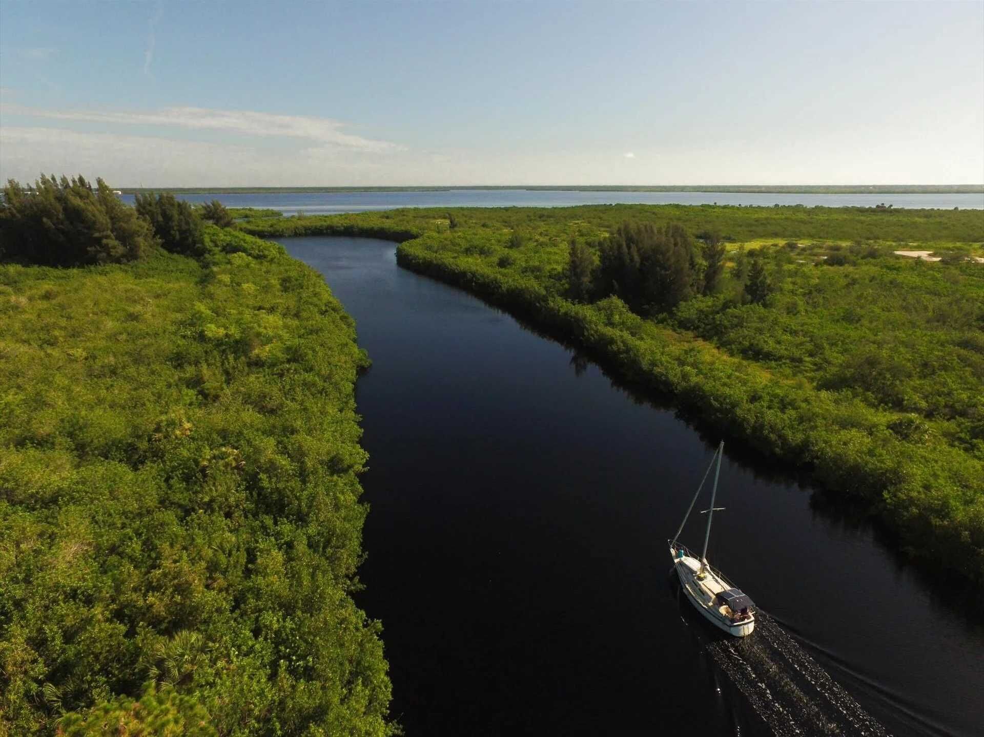 Un étroit canal bordé d’une végétation luxuriante, dans lequel une petite embarcation navigue.