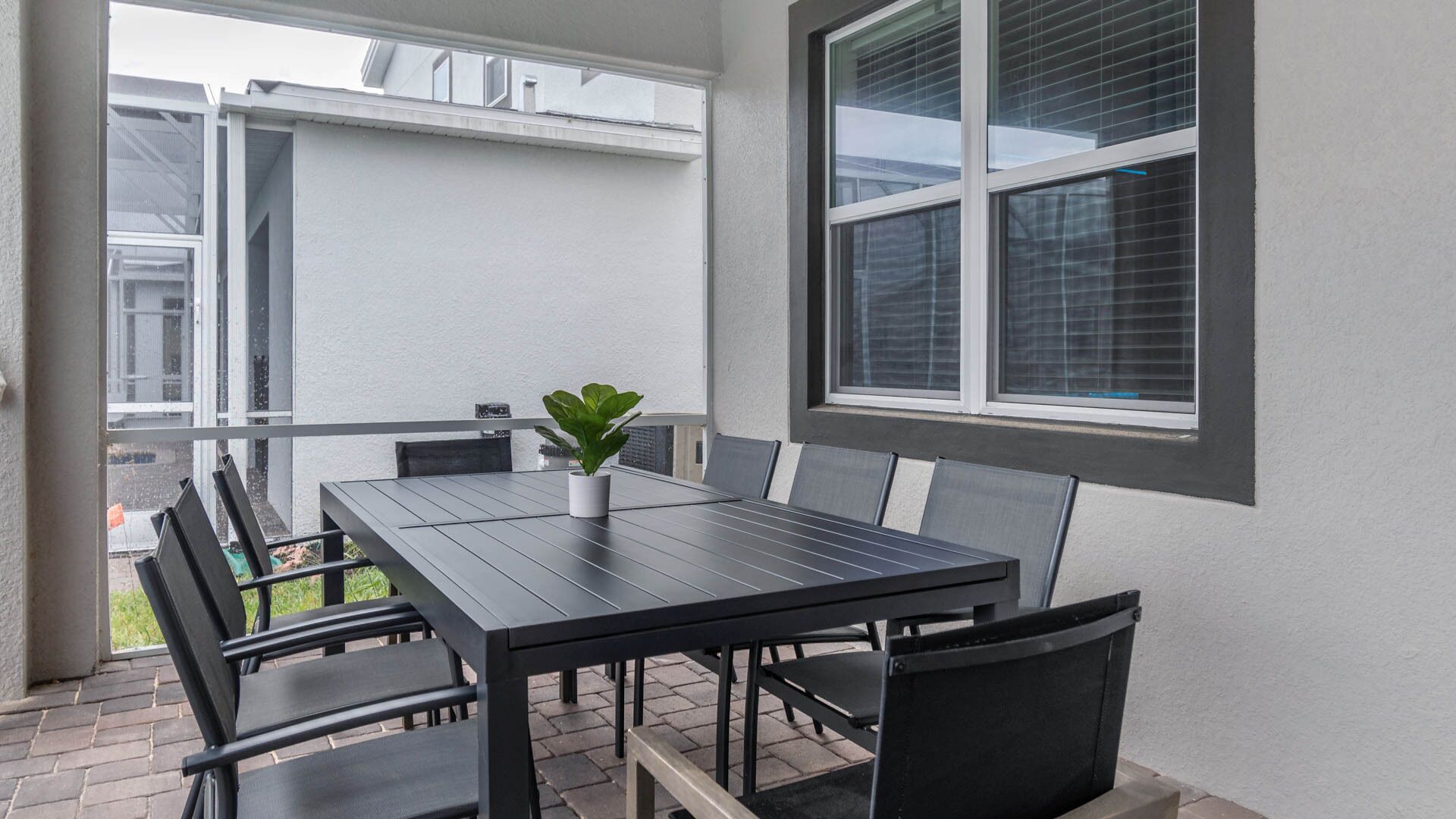 Un patio con mesa y sillas, una planta en maceta y una ventana con persianas.