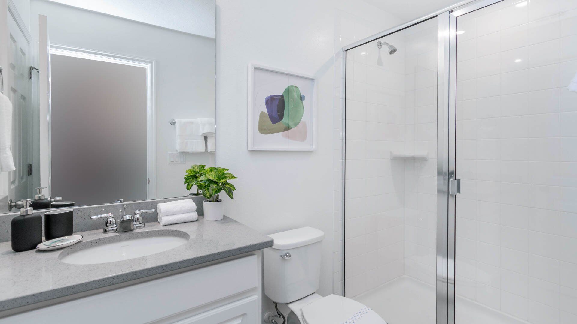 A modern bathroom with a large mirror, two sinks, a toilet, and a glass shower enclosure.