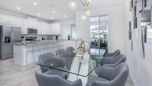 A modern kitchen with white cabinets, stainless steel appliances, and a glass dining table with grey chairs. - ADT8976 Summary:<br>Sola (Kissimmee)