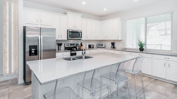 A modern kitchen with white cabinets, stainless steel appliances, and a large island with clear bar stools. - ADT8976 Summary:<br>Sola (Kissimmee)