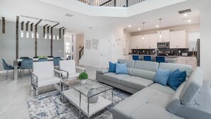 A modern living room with a grey sofa, white chairs, a glass coffee table, and a dining area with a white table and blue chairs. - WSB610 Summary:<br>Champ (Kissimmee)