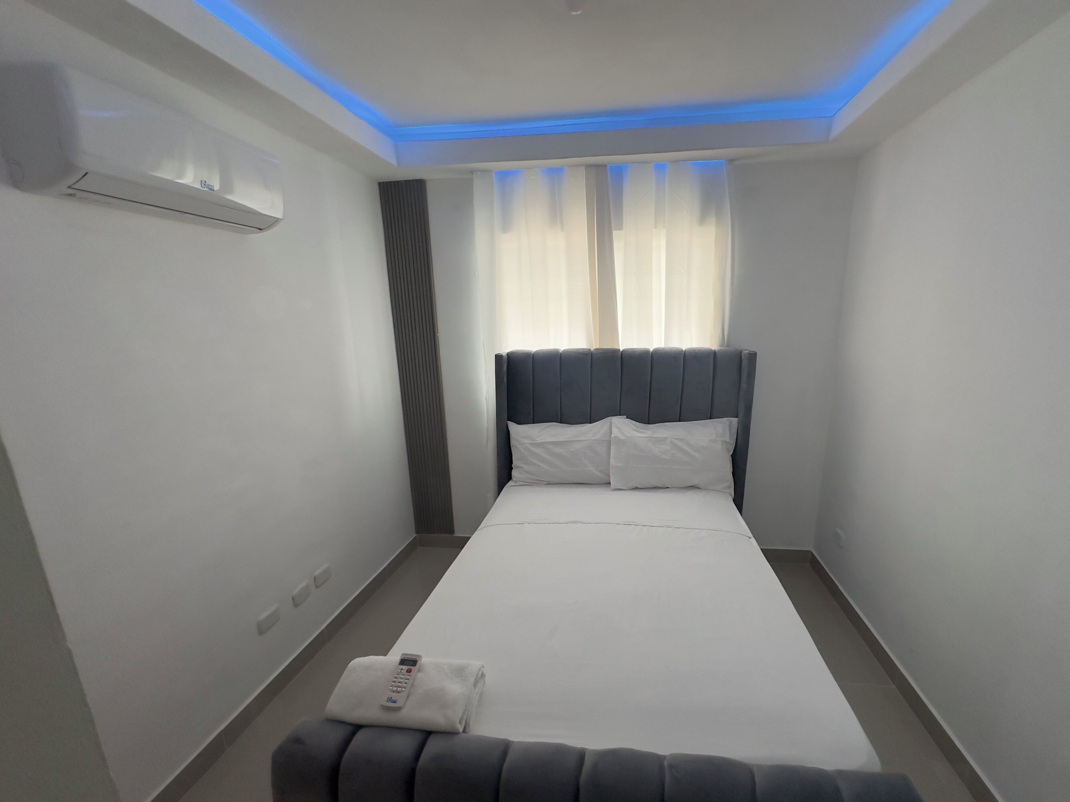Une chambre d’hôtel avec un lit, une table de chevet, une télécommande et une fenêtre avec des rideaux.