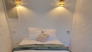 Een slaapkamer met een tegelvloer, een bed met wit en groen beddengoed, en twee wandlampen.