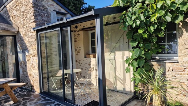 Een stenen huis met een glazen patio, een houten tafel en een potplant.