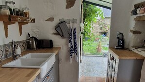 Een keuken met betegelde vloer, houten aanrecht, een spoelbak en een raam met uitzicht op een tuin.
