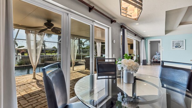 A spacious patio with a glass table and chairs, a pool, and a ceiling fan.