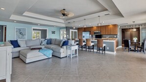 A spacious living area with a large L-shaped sofa, a dining area with a kitchen island, and a ceiling fan.