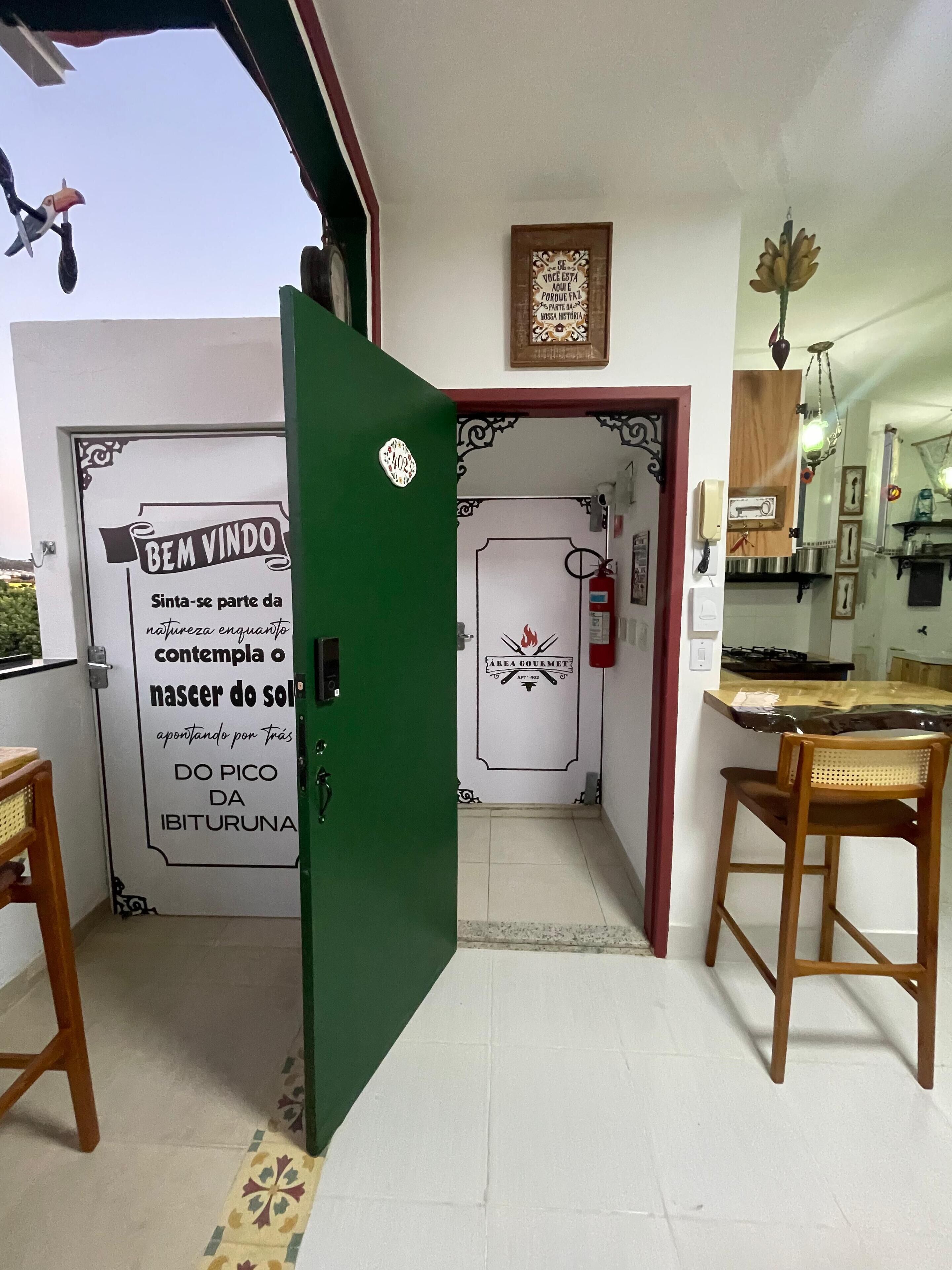 Una habitación con puerta verde, área de cocina y comedor con dos sillas de madera.