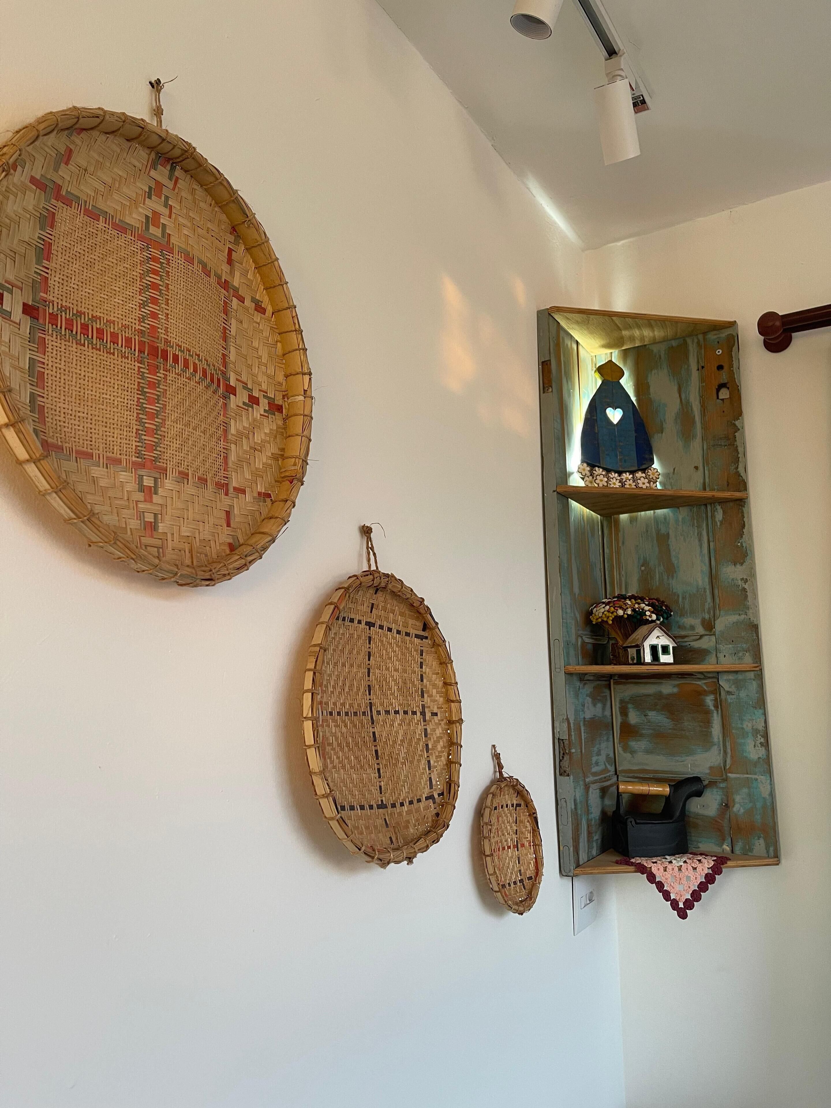 Een muur met drie geweven manden in verschillende maten en een rustieke plank met decoratieve objecten.
