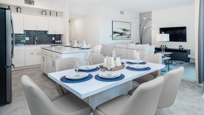 Une cuisine moderne avec des meubles blancs, un îlot central et un coin repas agrémenté d’une table blanche dressée pour six personnes.