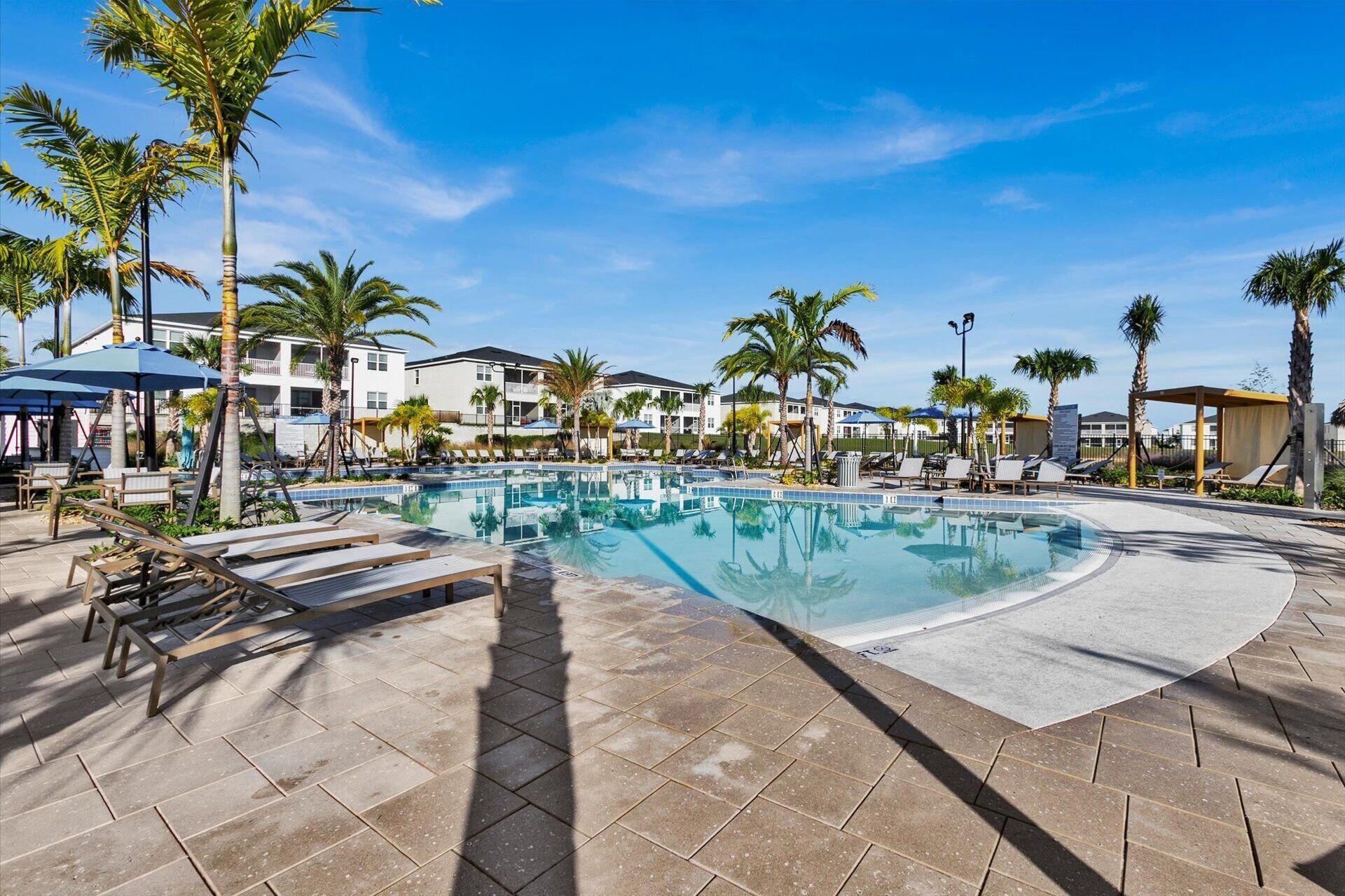 A swimming pool with lounge chairs and palm trees, surrounded by buildings.