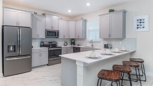 A modern kitchen with stainless steel appliances, grey cabinets, a central island with stools, and a microwave above the stove. - NRL4543 Summary:<br>Stor (Kissimmee)
