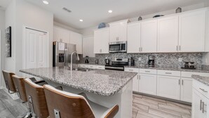 A modern kitchen with white cabinets, granite countertops, stainless steel appliances, and a central island with bar stools. - KCC 4797 Summary:<br>Sto (Kissimmee)