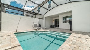A swimming pool with a clear blue water, surrounded by a stone patio. There are lounge chairs and a table with chairs. - Cbp2166 (Kissimmee)