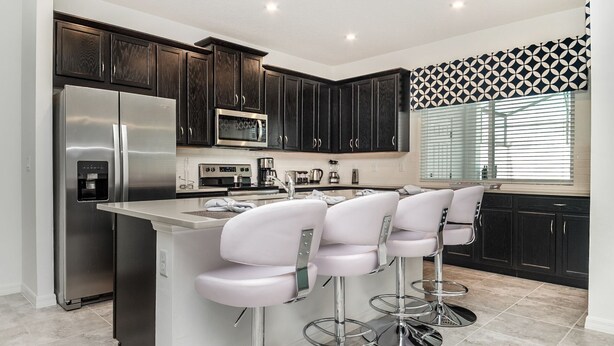 A modern kitchen with dark wood cabinets, stainless steel appliances, and a central island with bar stools. - Cbp2166 (Kissimmee)