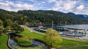 Un puerto deportivo con barcos amarrados, un pequeño estanque y un puente que conecta con una comunidad en una ladera.