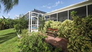 A modern house with a glass-enclosed patio, a swimming pool, and lush greenery. - Vgd27305 (Punta Gorda)