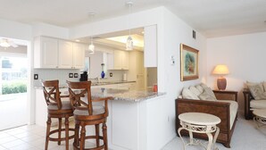 A modern kitchen with white cabinets, a marble countertop, and a dining area with wooden chairs. - Vgd27305 (Punta Gorda)