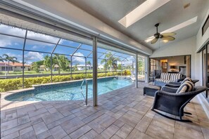 Un vaste espace intérieur abritant une piscine, offrant une vue dégagée sur le quartier environnant, doté d’un ventilateur de plafond et d’un coin salon avec un canapé et des fauteuils.