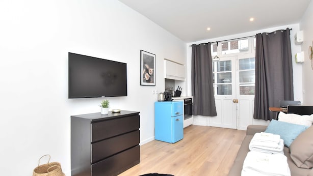 Un salon moderne avec un téléviseur à écran plat, un réfrigérateur bleu, un canapé avec un coussin bleu et une fenêtre avec des rideaux.