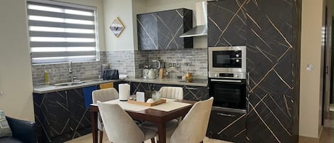 A modern kitchen with a dining area, featuring a marble backsplash, built-in appliances, and a dining table with chairs.
