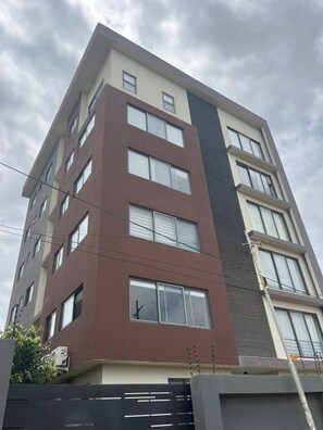 A multi-story building with a modern architectural design, featuring a combination of brown and beige exterior walls, large windows, and a visible air conditioning unit. - Modern, well fitted, enjoyable apartment with AC in vibrant Osu, off Oxford St. (Accra)