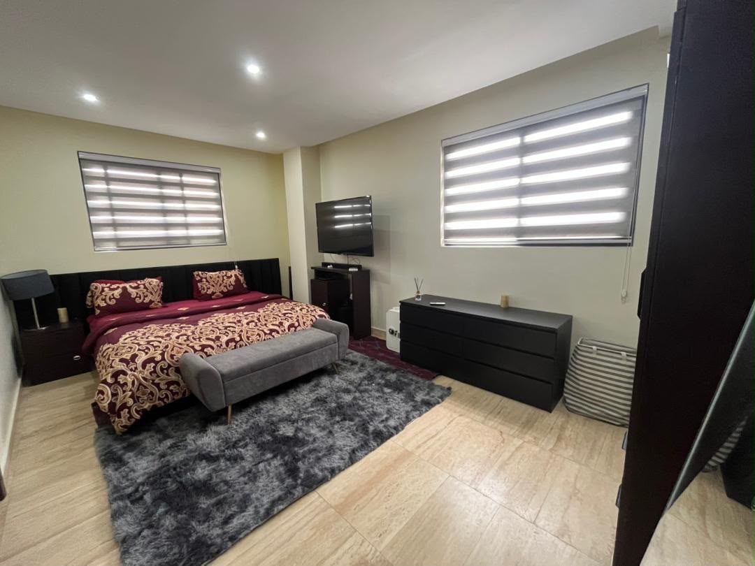 A bedroom with a bed, bedside tables, a TV, a dresser, and a window with blinds.